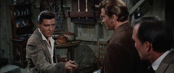 Movie still from “Flaming Star” (1960), directed by Don Siegel – Two men are talking in a kitchen with a knife in their hand; Medium shot, Over the shoulder angle