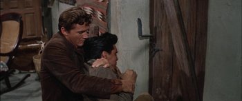 Movie still from “Flaming Star” (1960), directed by Don Siegel – A man and a woman hug in front of an open door; Medium shot, Over the shoulder angle