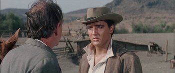 Movie still from “Flaming Star” (1960), directed by Don Siegel – A man wearing a cowboy hat talking to another man; Close Up shot, Over the shoulder angle