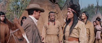 Movie still from “Flaming Star” (1960), directed by Don Siegel – A group of men standing next to each other in front of a building; Medium shot, Over the shoulder angle