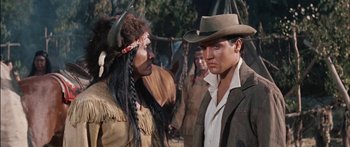 Movie still from “Flaming Star” (1960), directed by Don Siegel – A man in a cowboy hat talking to an indian; Medium shot, Over the shoulder angle