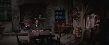 Movie still from “Flaming Star” (1960), directed by Don Siegel – A man sitting at a wooden table in a dark room; Wide shot, High angle