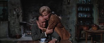 Movie still from “Flaming Star” (1960), directed by Don Siegel – A man and a woman sitting at a wooden table; Medium shot, Low angle