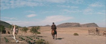 Movie still from “Flaming Star” (1960), directed by Don Siegel – A man riding on the back of a brown horse down a dirt road; Extreme Wide shot, High angle