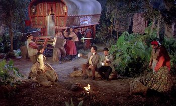 Movie still from “Frankie and Johnny” (1966), directed by Frederick De Cordova – A group of people sitting on the ground next to a fire pit; Wide shot, High angle