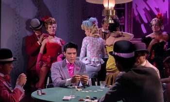Movie still from “Frankie and Johnny” (1966), directed by Frederick De Cordova – A man sitting at a table in front of a group of people; Medium shot, Over the shoulder angle
