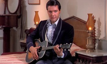 Movie still from “Frankie and Johnny” (1966), directed by Frederick De Cordova – A man sitting on top of a bed holding a guitar; Medium shot, Low angle