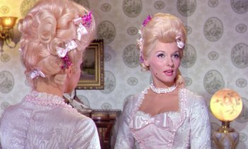 Movie still from “Frankie and Johnny” (1966), directed by Frederick De Cordova – A woman with long blonde hair and pink flowers in her hair looking at herself in the mirror; Medium shot, Over the shoulder angle