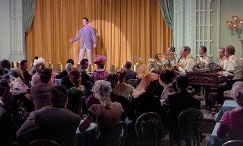 Movie still from “Frankie and Johnny” (1966), directed by Frederick De Cordova – A man standing in front of an audience and a band; Wide shot, Over the shoulder angle