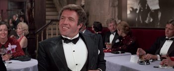 Movie still from “Funny Lady” (1975), directed by Herbert Ross – A man in a tuxedo smiling for the camera at an event; Medium shot, Low angle