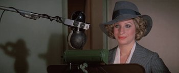 Movie still from “Funny Lady” (1975), directed by Herbert Ross – A woman wearing a hat is standing next to a microphone; Close Up shot, High angle