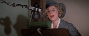 Movie still from “Funny Lady” (1975), directed by Herbert Ross – A woman in a hat singing into a microphone; Close Up shot, High angle