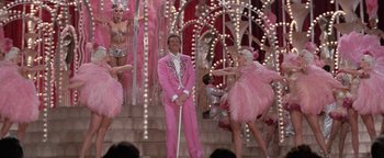 Movie still from “Funny Lady” (1975), directed by Herbert Ross – A man in a pink suit standing in front of a group of dancers; Wide shot, Low angle