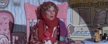 Movie still from “Funny Lady” (1975), directed by Herbert Ross – A woman sitting in a chair wearing a red scarf and holding a cup; Medium shot, High angle