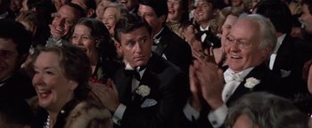 Movie still from “Funny Lady” (1975), directed by Herbert Ross – A crowd of people in suits clapping in front of a man; Medium shot, Over the shoulder angle