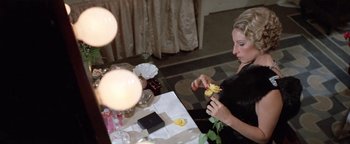 Movie still from “Funny Lady” (1975), directed by Herbert Ross – A woman sitting at a table with a flower in her hand; Close Up shot, High angle