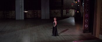 Movie still from “Funny Lady” (1975), directed by Herbert Ross – A woman in a black dress standing in a dark room; Wide shot, High angle