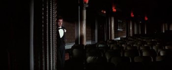 Movie still from “Funny Lady” (1975), directed by Herbert Ross – A man in a tuxedo standing in front of a wall of chairs; Wide shot, Low angle