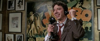 Movie still from “Funny Lady” (1975), directed by Herbert Ross – A man in a suit and tie holding up a phone; Close Up shot, Low angle