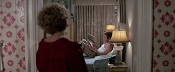 Movie still from “Funny Lady” (1975), directed by Herbert Ross – A man sitting on a bed reading a book while a woman watches; Medium shot, Over the shoulder angle