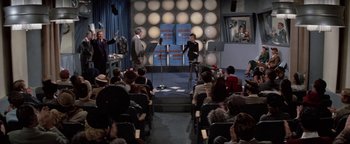 Movie still from “Funny Lady” (1975), directed by Herbert Ross – A group of people sitting in front of microphones in a room; Wide shot, High angle