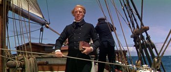 Movie still from “Hawaii” (1966), directed by George Roy Hill – A man holding a book while standing next to a boat; Medium shot, Low angle
