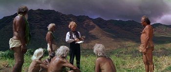 Movie still from “Hawaii” (1966), directed by George Roy Hill – A group of people sitting in the grass near a mountain; Wide shot, High angle