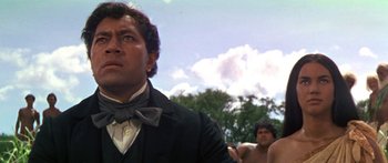 Movie still from “Hawaii” (1966), directed by George Roy Hill – A man wearing a suit and bow tie in front of a group of shirtless men; Close Up shot, Low angle