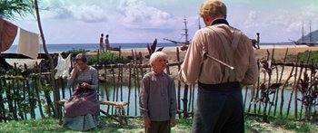 Movie still from “Hawaii” (1966), directed by George Roy Hill – A young boy standing next to an older man in front of a body of water; Wide shot, Over the shoulder angle