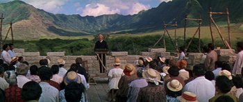 Movie still from “Hawaii” (1966), directed by George Roy Hill – A man is giving a speech to a group of people in front of a mountain range; Extreme Wide shot, Over the shoulder angle