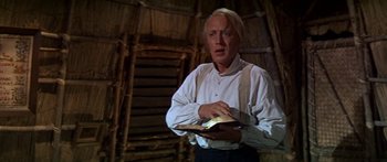 Movie still from “Hawaii” (1966), directed by George Roy Hill – A man holding a book while standing next to a wall; Close Up shot, Low angle
