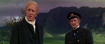 Movie still from “Hawaii” (1966), directed by George Roy Hill – Two men standing next to each other in front of mountains; Medium shot, Low angle