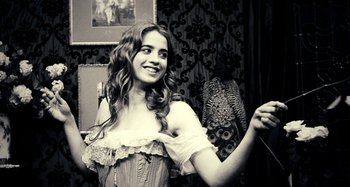 Movie still from “House of Tolerance” (2011), directed by Bertrand Bonello – A woman in a corset smiling for the camera; Medium shot, Low angle