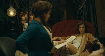 Movie still from “House of Tolerance” (2011), directed by Bertrand Bonello – Two women sitting on a red couch in a room; Medium shot, Over the shoulder angle
