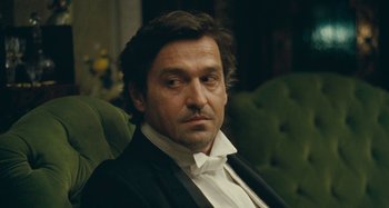 Movie still from “House of Tolerance” (2011), directed by Bertrand Bonello – A person sitting in a chair wearing a suit; Close Up shot, Low angle