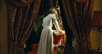 Movie still from “House of Tolerance” (2011), directed by Bertrand Bonello – A woman in a white dress standing in front of a chair; Wide shot, High angle