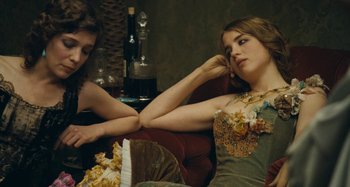 Movie still from “House of Tolerance” (2011), directed by Bertrand Bonello – Two women sitting on a red couch next to each other; Medium shot, Over the shoulder angle