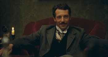 Movie still from “House of Tolerance” (2011), directed by Bertrand Bonello – A man sitting in a chair wearing a suit and tie; Close Up shot, Low angle