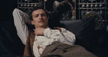 Movie still from “House of Tolerance” (2011), directed by Bertrand Bonello – A man laying on a couch with his eyes closed; Medium shot, High angle