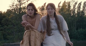 Movie still from “House of Tolerance” (2011), directed by Bertrand Bonello – Two young women sitting next to each other on the grass; Medium shot, Low angle
