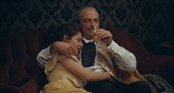 Movie still from “House of Tolerance” (2011), directed by Bertrand Bonello – An older man and a young woman drinking wine; Medium shot, Low angle