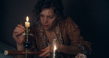 Movie still from “House of Tolerance” (2011), directed by Bertrand Bonello – A woman sitting in front of a lit candle in a room; Close Up shot, High angle
