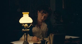 Movie still from “House of Tolerance” (2011), directed by Bertrand Bonello – A woman sitting at a table writing on a piece of paper next to a lamp; Medium shot, High angle