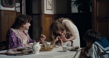 Movie still from “House of Tolerance” (2011), directed by Bertrand Bonello – Two women and a child are sitting at a dinner table; Medium shot, Over the shoulder angle