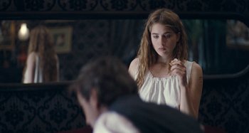 Movie still from “House of Tolerance” (2011), directed by Bertrand Bonello – A young woman eating a piece of food in front of a mirror; Medium shot, Over the shoulder angle