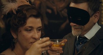 Movie still from “House of Tolerance” (2011), directed by Bertrand Bonello – A man and a woman wearing a black mask and holding drinks; Close Up shot, Over the shoulder angle