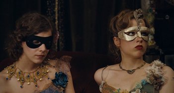 Movie still from “House of Tolerance” (2011), directed by Bertrand Bonello – Two women sitting on a couch wearing masks and jewelry; Close Up shot, Over the shoulder angle