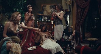 Movie still from “House of Tolerance” (2011), directed by Bertrand Bonello – A group of people sitting around a living room; Wide shot, High angle