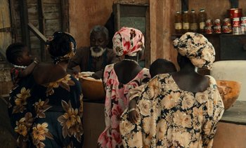 Movie still from “Hyenas” (1992), directed by Djibril Diop Mambéty – A group of people standing around a table; Medium shot, High angle