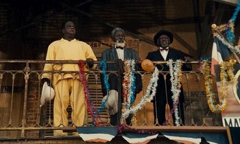 Movie still from “Hyenas” (1992), directed by Djibril Diop Mambéty – A group of men standing next to each other on top of a railing; Wide shot, Low angle
